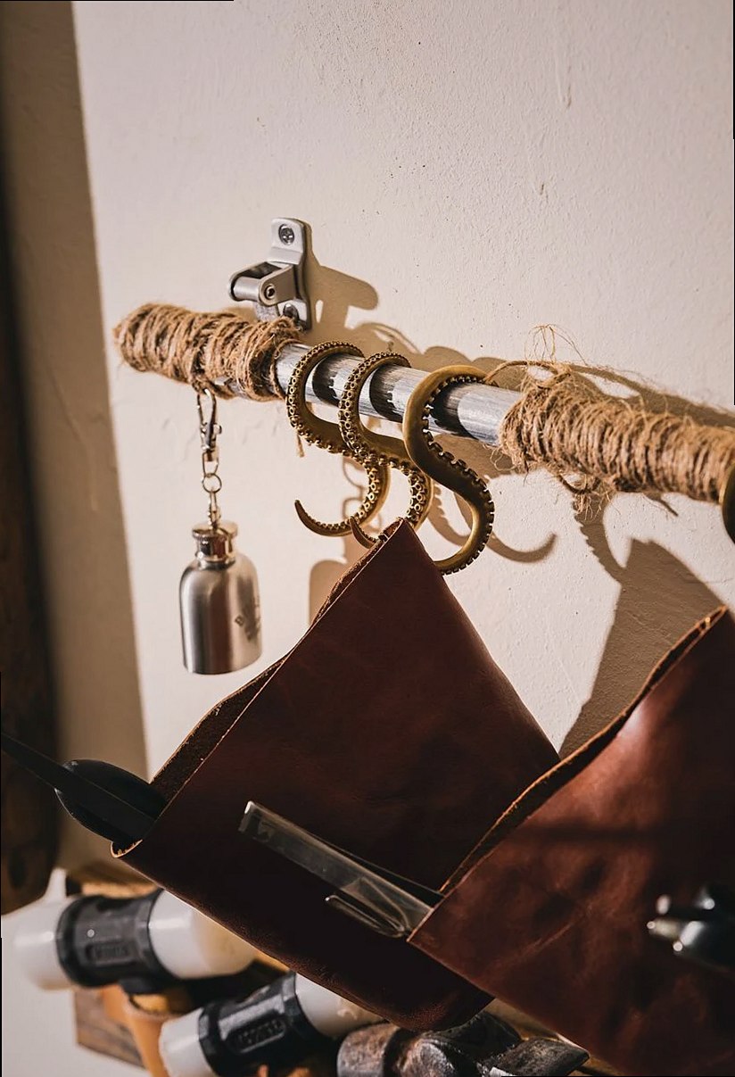 Close-up of vintage leather tool bags hanging on ornate, brass octopus tentacle hooks against a wall.